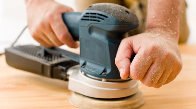 man sanding wooden floor in workshop