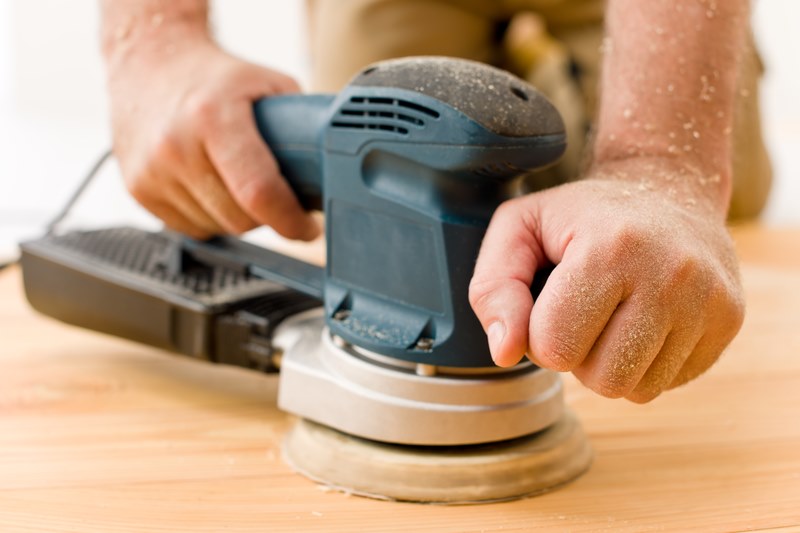 man sanding wooden floor in workshop