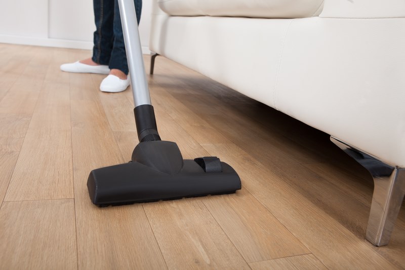 Low section of woman vacuuming hardwood floor at home