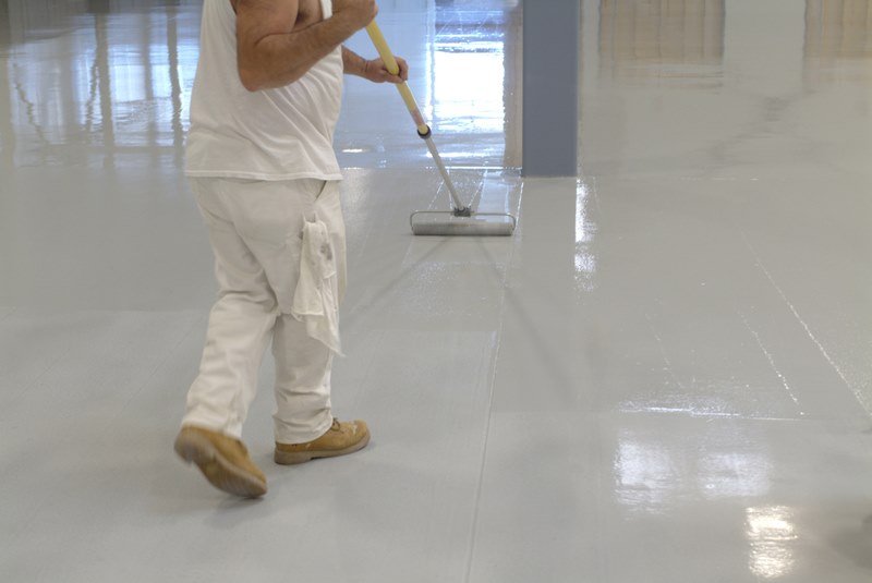 a worker rolls an epoxy paint onto a new warehouse floor